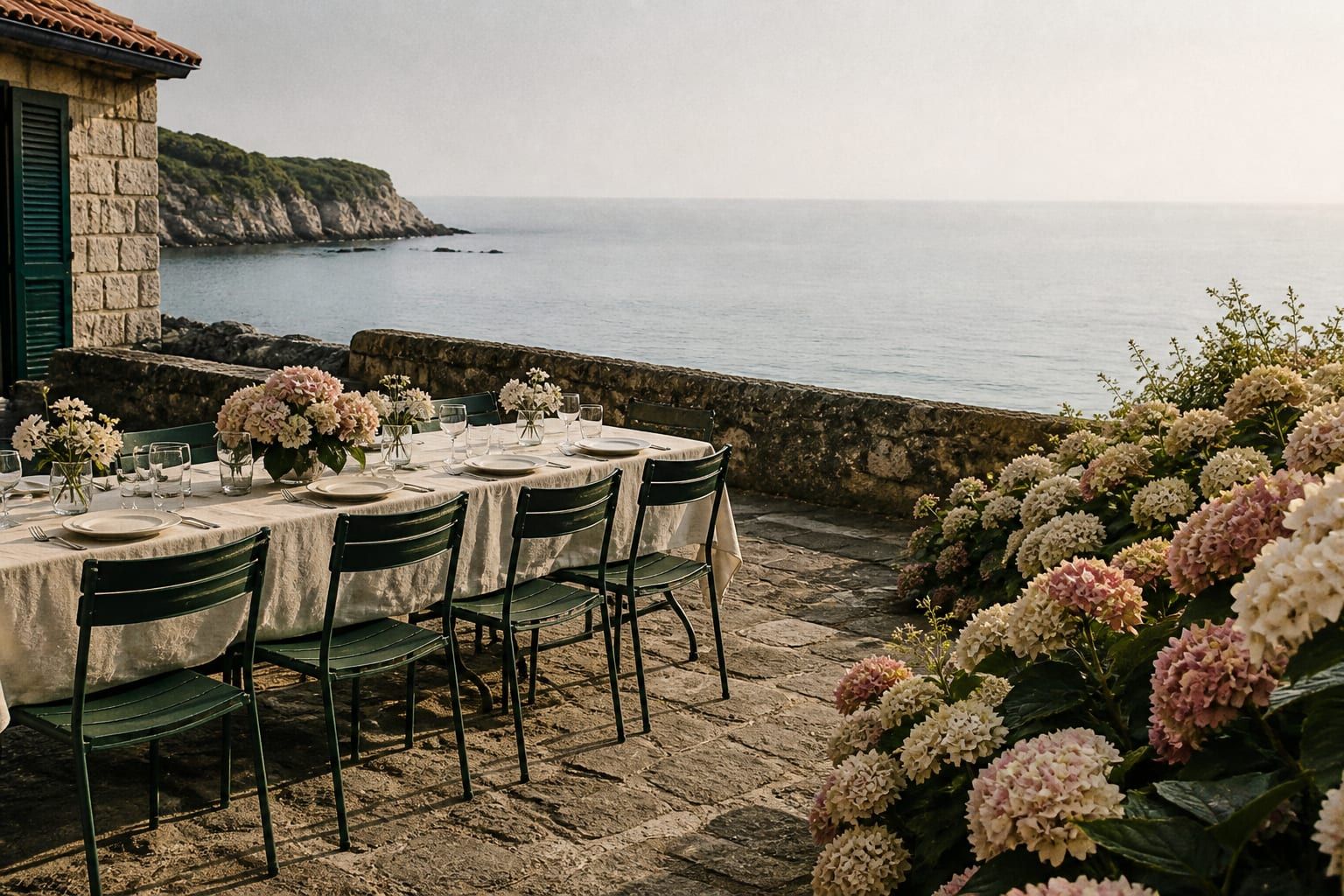 Empty stone terrace above the Atlantic in long June light, hydrangeas at the edge